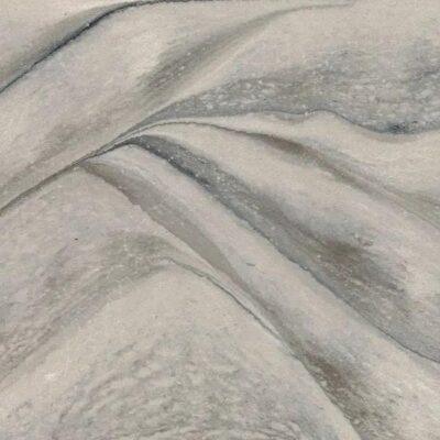 Close-up of sand dunes with soft curves and shadows, creating a textured, abstract landscape pattern.
