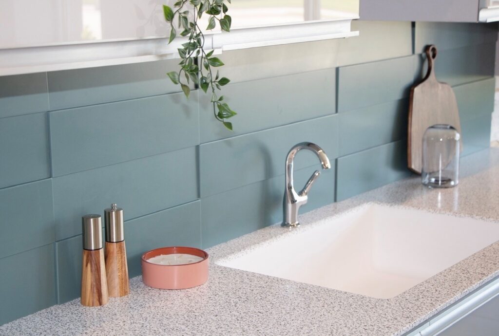 Modern kitchen countertop with a sink, faucet, salt and pepper shakers, plant, and cutting board.
